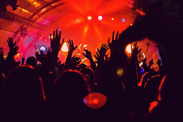 Fototapeta na wymiar Abstract blur atmosphere: happy people enjoying outdoor music festival concert, raised up hands and clapping of pleasure, active night life concept, play of light and shadow on the stage
