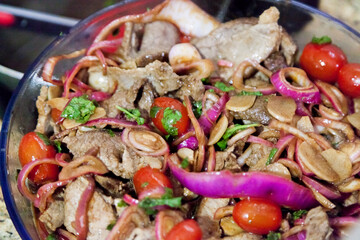 Preparing a roast beef lunch in a Brazilian cuisine, with red onions, cherry tomatoes and more spices and also using a red tongs to facilitate the cooking of the meat. Cooking concept. Food concept
