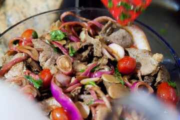 Preparing a roast beef lunch in a Brazilian cuisine, with red onions, cherry tomatoes and more spices and also using a red tongs to facilitate the cooking of the meat. Cooking concept. Food concept
