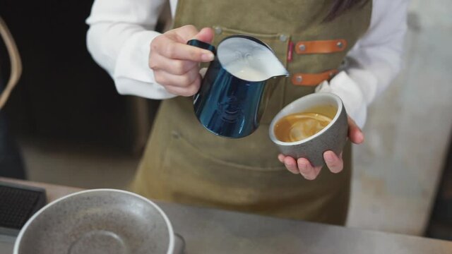 Closeup barista hand pouring steamed milk into hot latte art coffee.