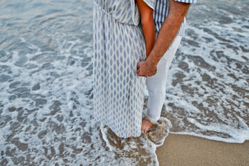 Close-up cropped image of a loving young couple on the seashore, holding hands enjoying each other and their vacation, romantically spending time on the beach.