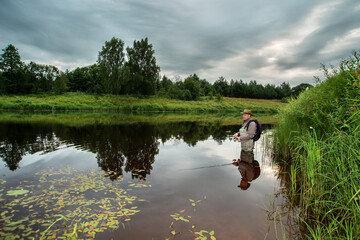 A fisherman, going shallow in the water, catches a fish on a spinning rod.