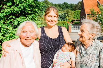 Two happy great grandmothers with granddaughter and newborn great granddaughter baby outdoors