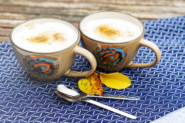 Two cups of cappuccino or latte with brown sugar and cinnamon. Coffee for two on a rustic table outside. Fall season beauty.