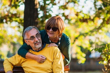 Naklejka na ściany i meble Happy Senior couple embracing in autumn park. Elderly couple relaxing in park on sunny day.