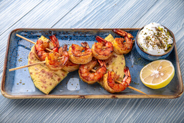 Souvlaki grilled shrimp on skewers. Natural delicious food. Greek cuisine menu. Still life in a marine style on a blue background.