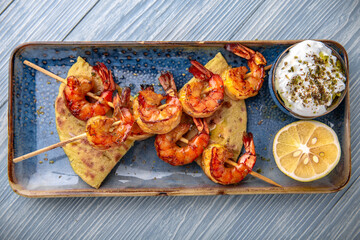 Souvlaki grilled shrimp on skewers. Natural delicious food. Greek cuisine menu. Still life in a marine style on a blue background.