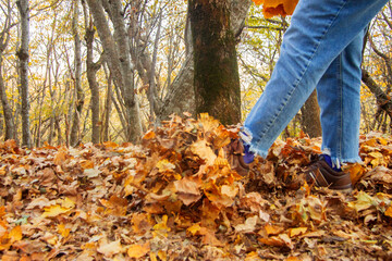 Womans leg kicks yellow autumn leaves from the ground in the park