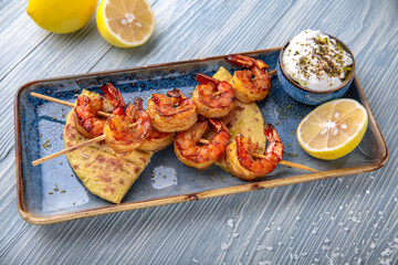 Souvlaki grilled shrimp on skewers. Natural delicious food. Greek cuisine menu. Still life in a marine style on a blue background.