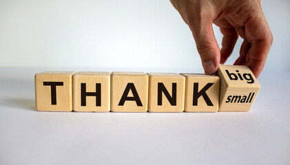 Male hand flips wooden cube and changes the inscription 'thank small' to 'thank big'. Beautiful white background, copy space.