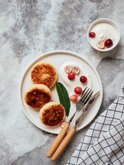 Cottage cheese pancakes on white plate with sour cream and berries on grey background. Homemade traditional Ukrainian and Russian syrniki. Healthy cheesecakes for breakfast. Vertical top view.