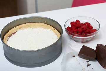 Coconut flakes in a biscuit with chocolate ganache. Nearby are raspberries with pieces of chocolate. Levington cake, stages of preparation.