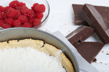 Coconut flakes in a biscuit with chocolate ganache. Nearby are raspberries with pieces of chocolate. Levington cake, stages of preparation.
