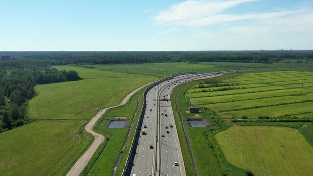 Asphalt ringroad. Speedway with cars through field near forest. Aerial view