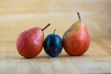 Group of pears and blue plums edible fruits, tasty ripened red yellow fruit on the table