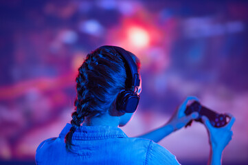 Streamer beautiful girl playing online video game with headphone and joystick. Sitting back. Neon...