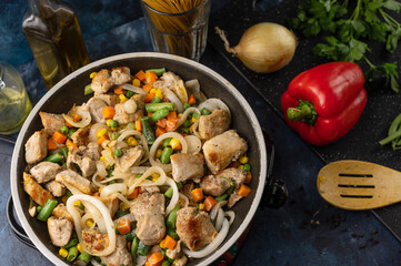 Top view of pan with frying pork meat with vegetables on dark blue background with ingredients for cooking traditional italian pasta. Food concept. Italian cuisine. Backstage of preparing dinner.