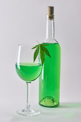 A glass and a bottle of green hemp-infused wine on white background