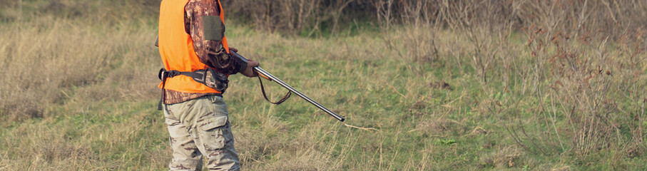 Duck hunter with shotgun walking through a meadow.