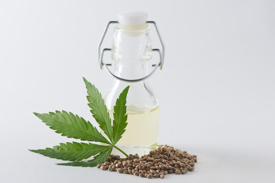 A bottle of hempseed oil with a hemp leaf and seeds on white background