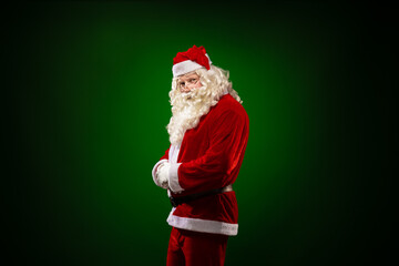 Emotional male actor in a costume of Santa Claus with a long beard gestures and poses on a green...
