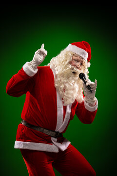Male actor in a costume of Santa Claus holds a microphone in his hands, sings and poses on a green background