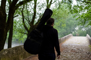 Young man carry guitar bag while walking through the forest