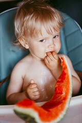 Happy toddler boy eating watermelon in his highchair