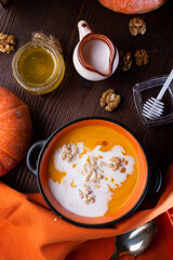 baked pumpkin cream coup with, walnuts ,  coconut milk and natural honey served in nice bowl. served at wooden brown table with ripe orange  pumkins. flat lay. healthy life concept