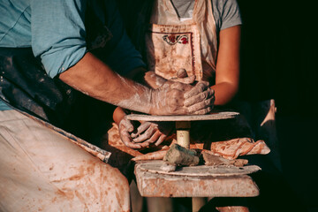 An experienced potter teaches an apprentice to work with clay and a potter's wheel