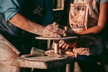 An experienced potter teaches an apprentice to work with clay and a potter's wheel