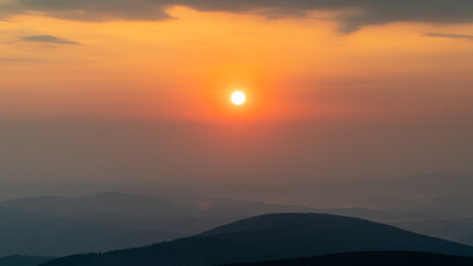 Photo of sunrise over mountains, beautiful orange-red light in the background. Morning fog over the peaks.