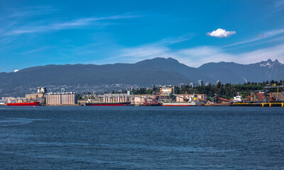 Obraz premium Ships under loading in the sea port of North Vancouver on the background of mountain range and blue sky