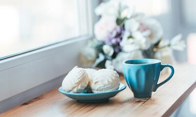 Morning breakfast of coffee and sweet marshmallows on wooden windowsill. Home comfort concept