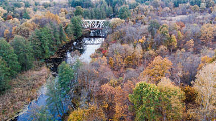 4K View from a quadcopter to a bridge over a river between reserved autumn forests along which the railway passes.