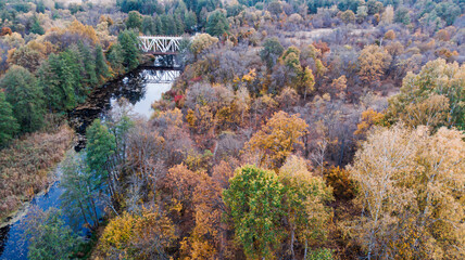 4K View from a quadcopter to a bridge over a river between reserved autumn forests along which the railway passes.
