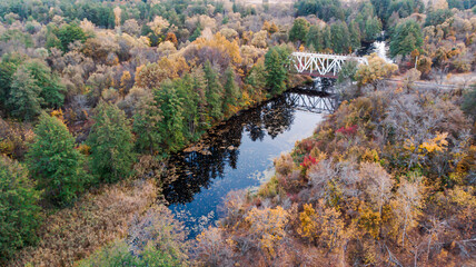 4K View from a quadcopter to a bridge over a river between reserved autumn forests along which the railway passes.