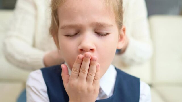 a sweet school girl yawns while mother combs hair. early rises to school.