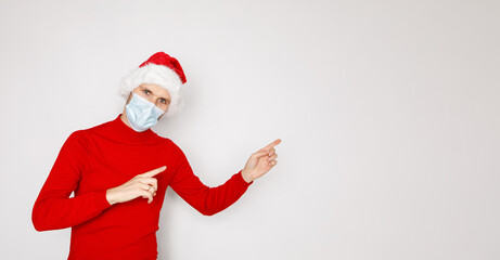 Christmas during pandemic of COVID-19 Coronavirus. Man wearing surgical face mask and Santa hat. Male model wearing red sweater on white isolated background. Place for copy banner text seasonal Sales