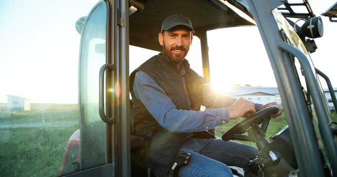 Portrait of young Caucasian male farmer in cap sitting in tractor with open door and smiling to camera. Field farming vehicle. Machine for agriculture. Handsome smiled man.