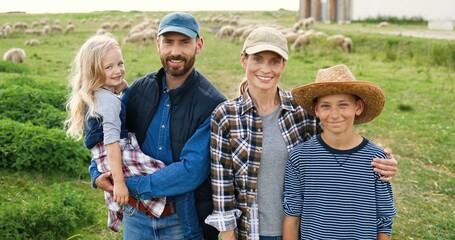 Portrait of Caucasian happy family with little kids standing at pasture with sheep flock on...