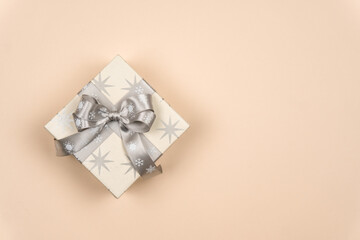 Christmas gift tied with a silver ribbon and bow on a delicate background with a place for the inscription of wishes