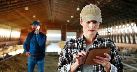 Young Caucasian happy pretty woman in hat using tablet device and smiling in farm stable. Portrait....