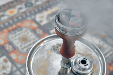 Embers on hookah bowl with smoke against traditional arabic style carpet