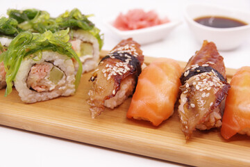 Japanese sushi food on a wooden tray, served with ginger, soy sauce and seaweed salad. Sushi rolls, salmon nigiri, shrimp nigiri, unagi nigiri