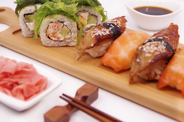 Japanese sushi food on a wooden tray, served with ginger, soy sauce and seaweed salad. Sushi rolls, salmon nigiri, shrimp nigiri, unagi nigiri