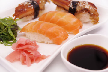 Japanese sushi food on a white plate, served with ginger and seaweed salad. Salmon nigiri, shrimp nigiri, unagi nigiri
