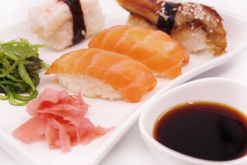 Japanese sushi food on a white plate, served with ginger and seaweed salad. Salmon nigiri, shrimp nigiri, unagi nigiri