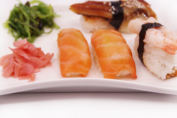 Japanese sushi food on a white plate, served with ginger and seaweed salad. Salmon nigiri, shrimp nigiri, unagi nigiri