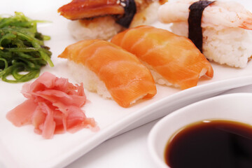 Japanese sushi food on a white plate, served with ginger and seaweed salad. Salmon nigiri, shrimp nigiri, unagi nigiri